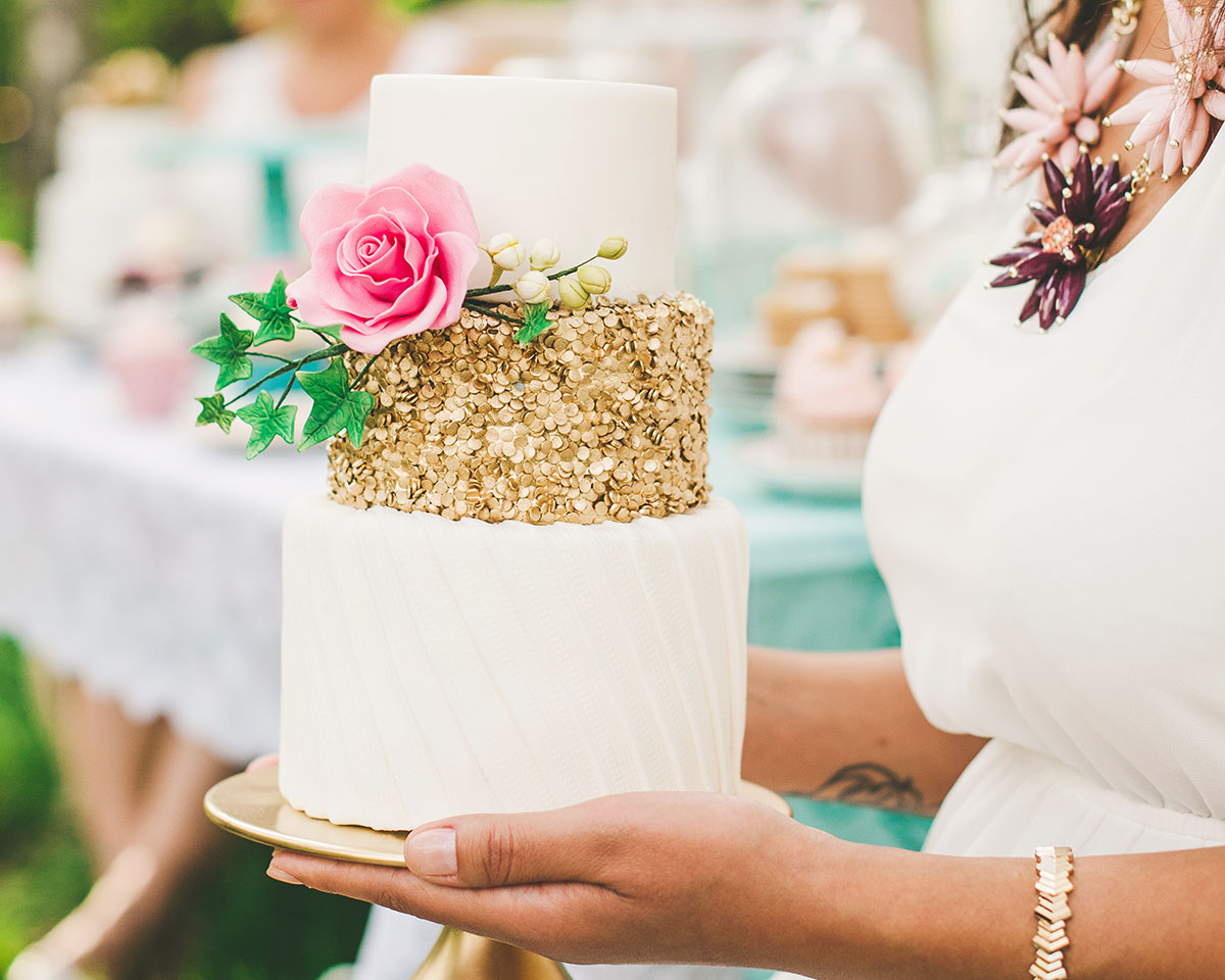 En brud håller i en vit bröllopstårta med guldiga detaljer